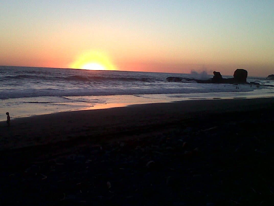 Surfers riding waves at El Tunco beach with dark volcanic sand