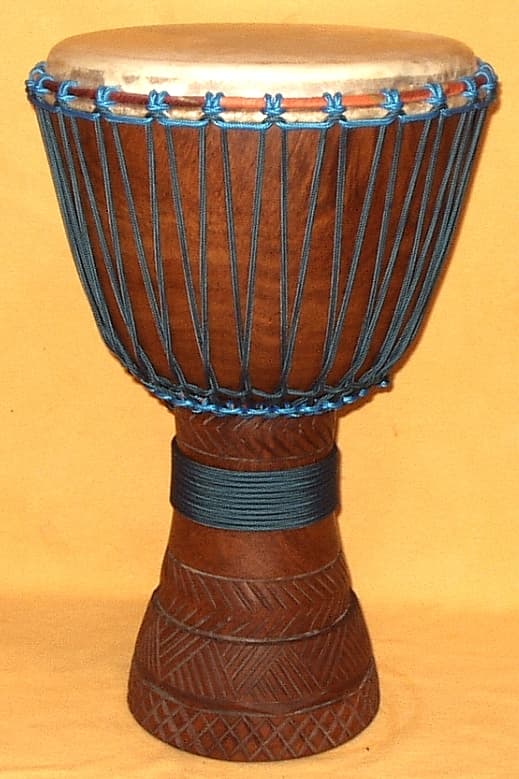 A circle of djembe drummers playing together outdoors in Mali, their hands a blur of motion