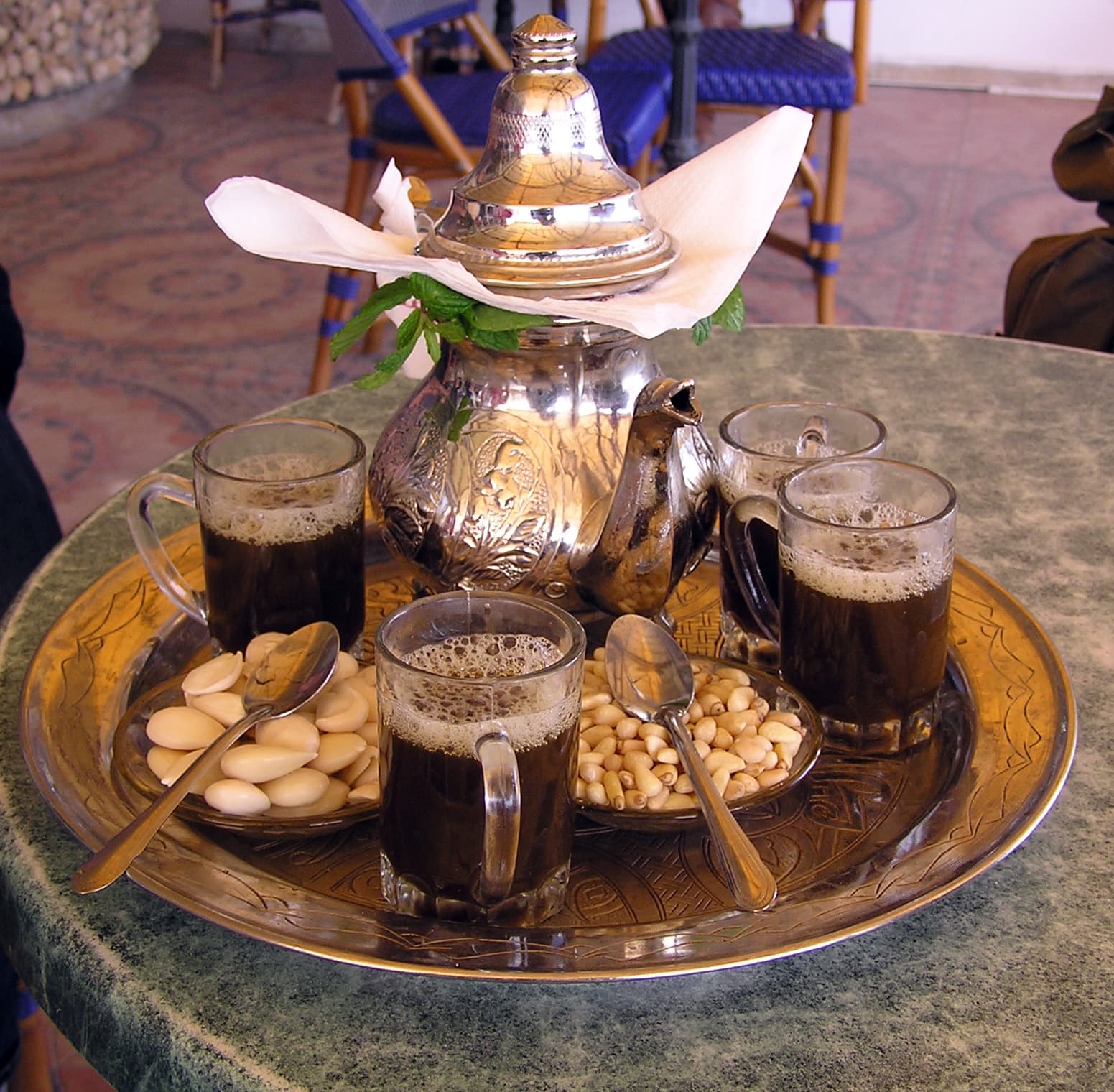 Small glasses of dark tea being poured from a height to create a froth on top
