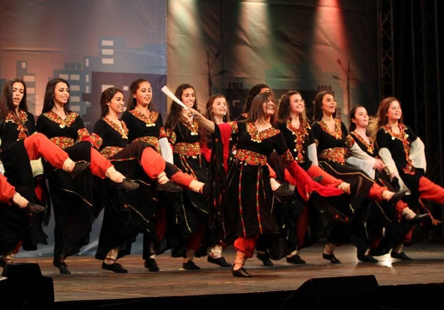 A line of dancers in traditional dress performing dabke with linked arms